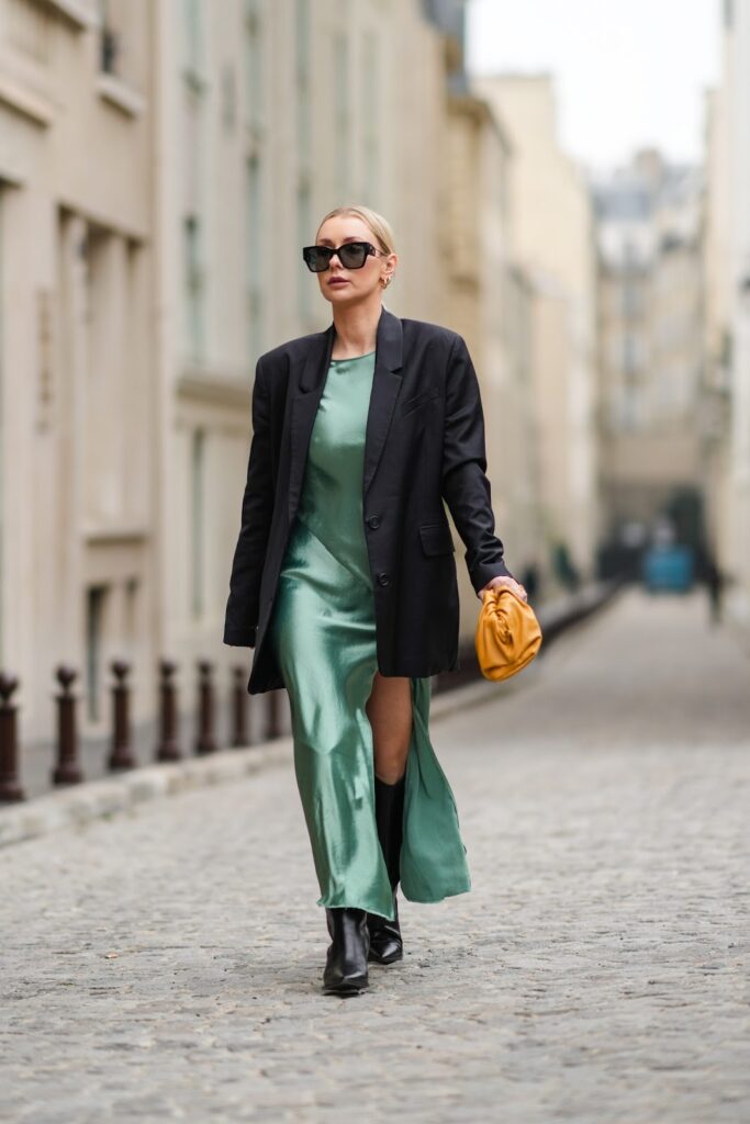 Frau in grünem Satinkleid, schwarzen Blazer, schwarzen Stiefeln und mit gelber Handtasche