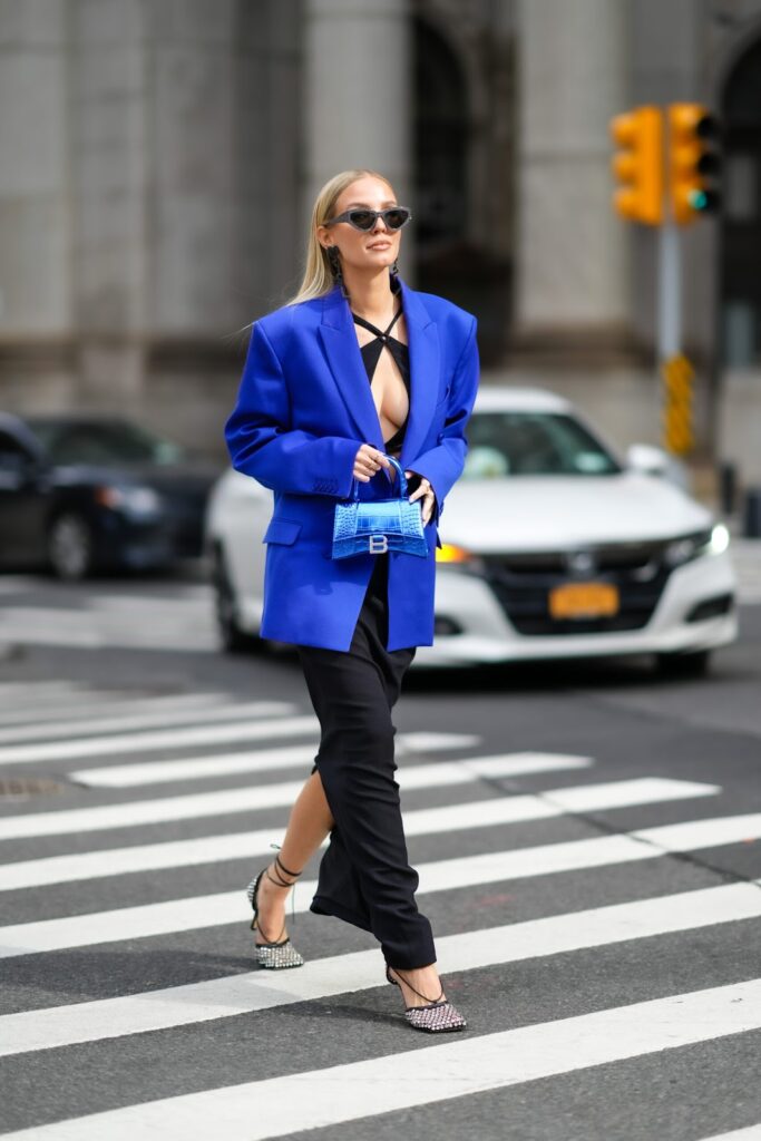 Frau in blauem Blazer, schwarzer Hose und mit blauer Handtasche geht durch die Straße