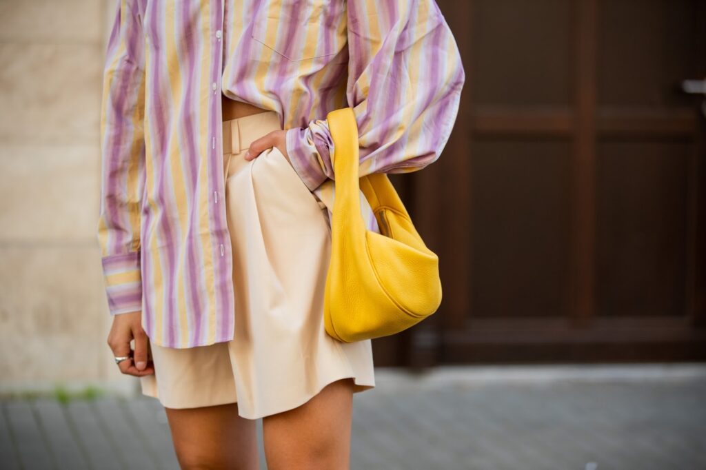 Trendsetterin in einem gemusterten, bunten Oversize-Hemd, einem neutralen Unterteil und einer kräftigen, farbenfrohen Handtasche