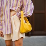 Trendsetterin in einem gemusterten, bunten Oversize-Hemd, einem neutralen Unterteil und einer kräftigen, farbenfrohen Handtasche