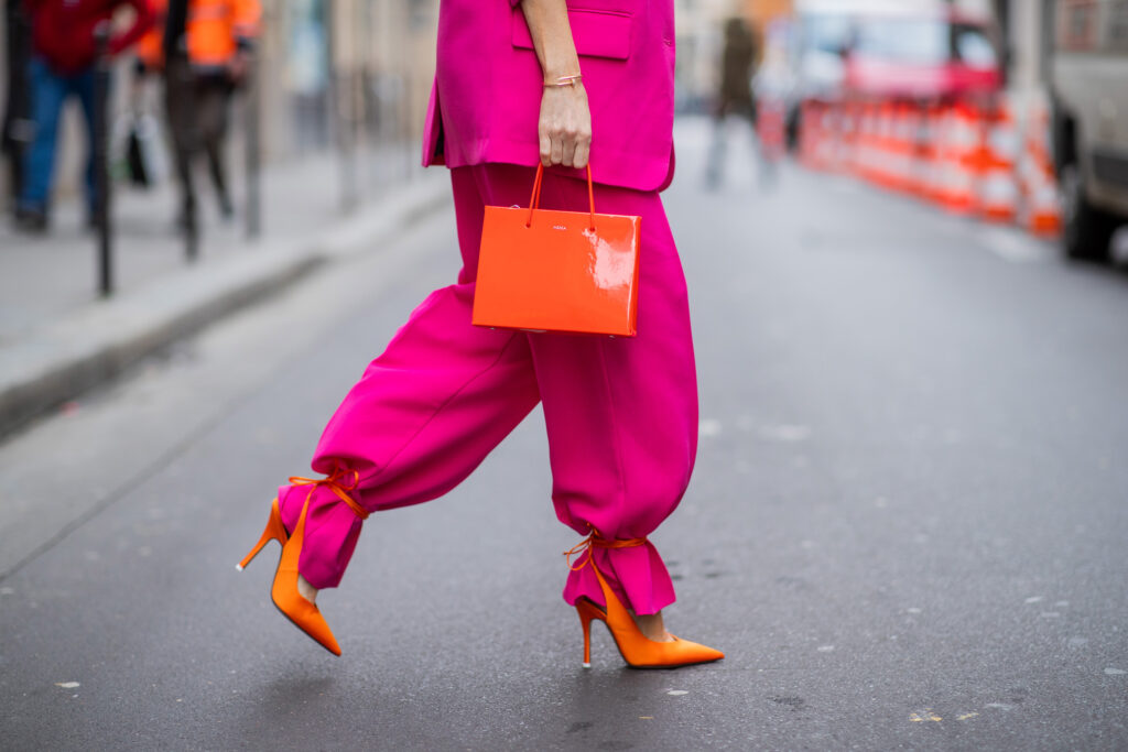 Frau in einem fuchsiafarbenen Damenzug, orangefarbenen Sandaletten und mit einer orangefarbenen Handtasche