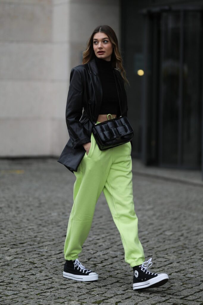Frau in einer grünen Hose, einem schwarzen Blazer und schwarzen Sneakers