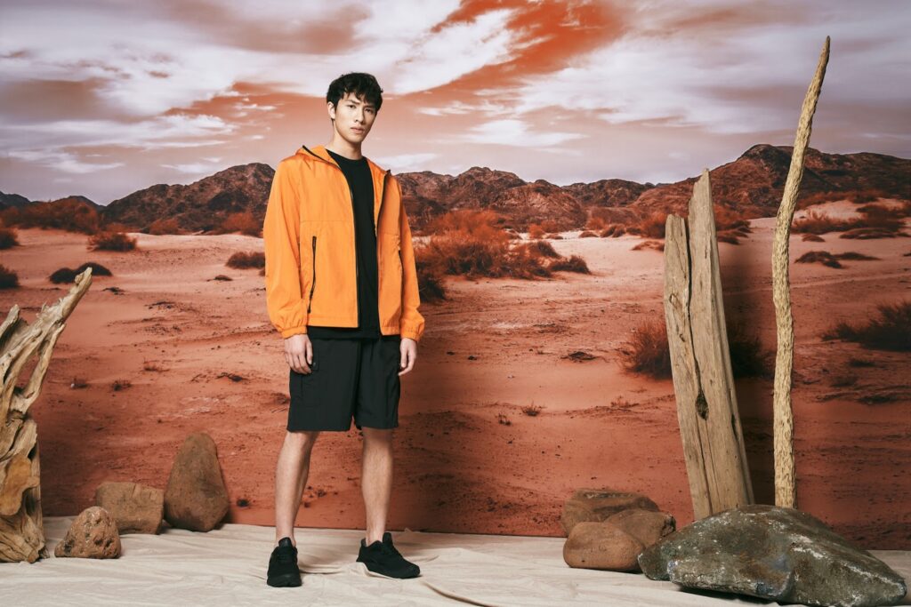 Mann in einem orangefarbenen Sweatshirt, in schwarzen Shorts und schwarzen Schuhen