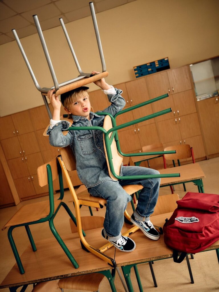 Junge im Denim-Look sitzt auf dem Tisch im Klassenraum