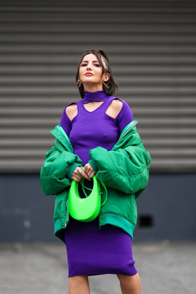 Frau im violettfarbenen Strickkleid, in grüner Bomberjacke und mit grüner Handtasche
