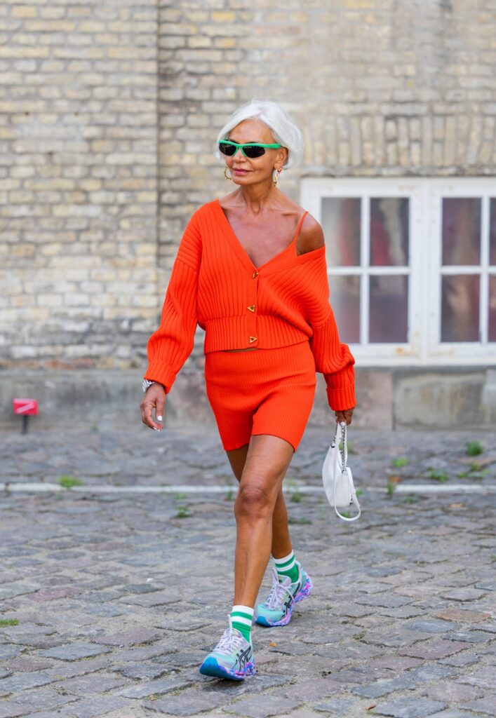 Frau im orangefarbenen Total-Look, mit einer weißen Handtasche und in Sneakers