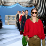 Foto von einer Modenschau, im Vordergrund ein Model in einem roten Pullover