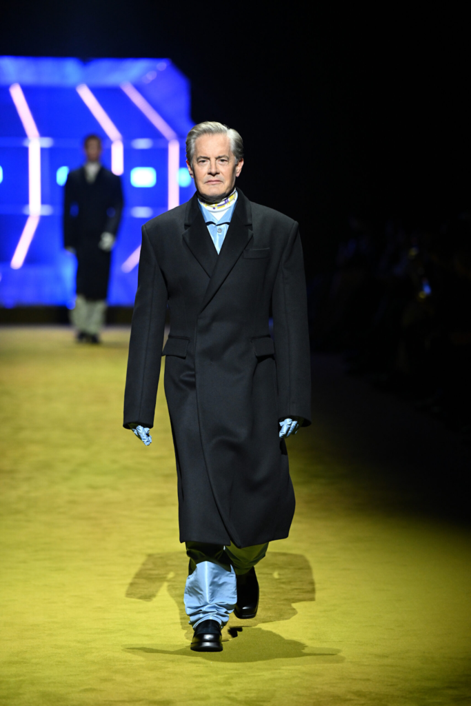 Mann im langen schwarzen Mantel, in einer glänzenden Hose und in Handschuhen