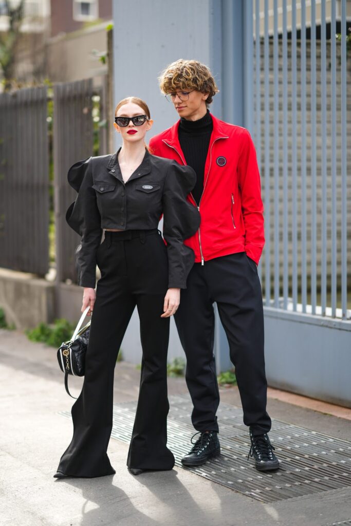Frau im schwarzen Total-Look und Mann im schwarzen Rollkragenpullover, in schwarzer Hose und roter Jacke