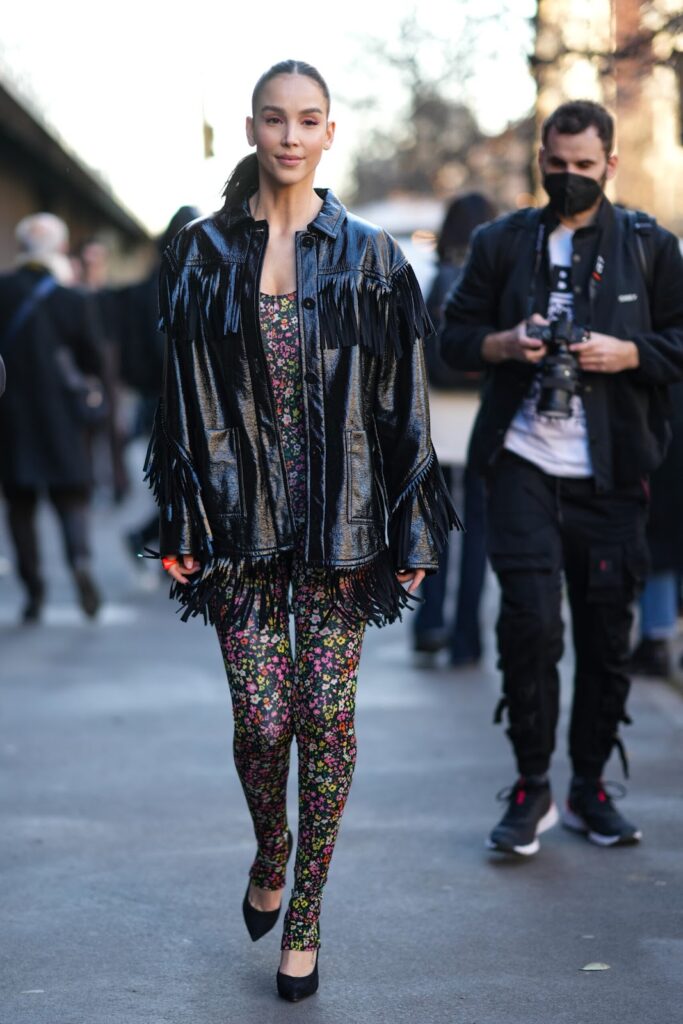 Frau in einer schwarzen Bikerjacke mit Fransen und im Jumpsuit mit floralem Muster