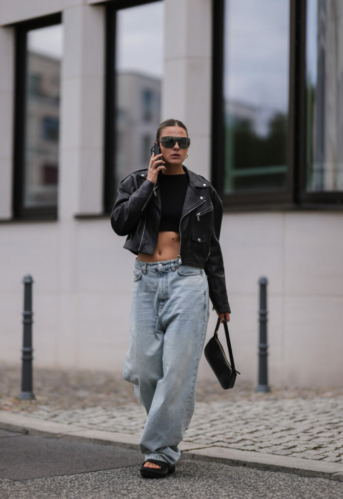 Frau in einer schwarzen Bikerjacke und Jeans mit kleiner Baguette Bag