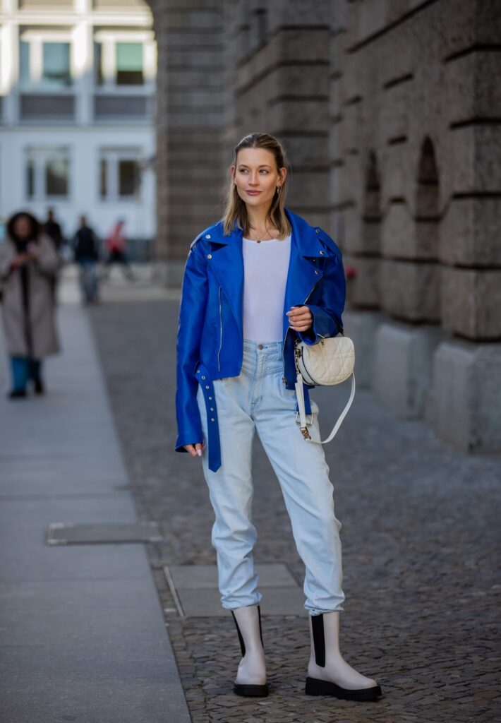  Frau in einer blauen Bikerjacke und Jeans mit mondförmiger Handtasche