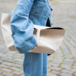 Frau im Denim-Look und mit einer beigefarbenen Handtasche