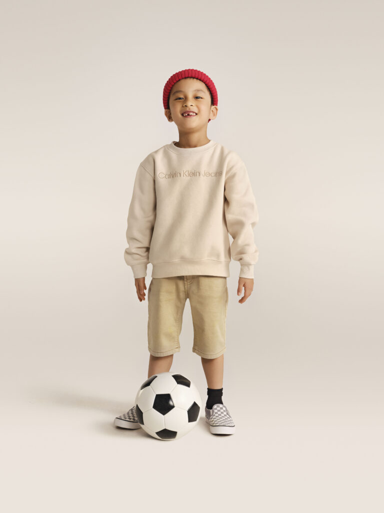 Ein Junge in Vans Schuhen und einem beigefarbenen Sweatshirt von Calvin Klein Jeans