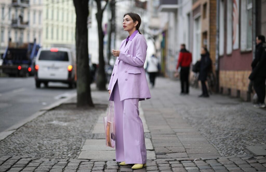 Eine junge Frau in einem lavendelfarbenen Damenanzug wartet auf dem Bürgersteig auf jemanden