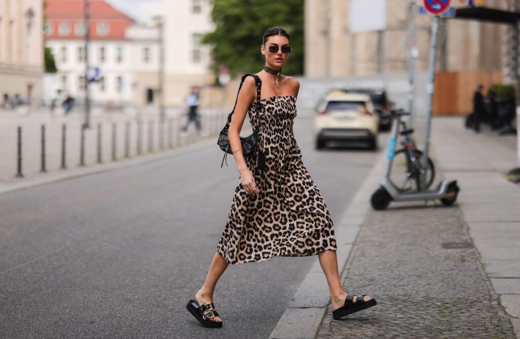 Eine junge Frau in einem leichten, luftigen Kleid mit Leopardenmuster überquert die Straße