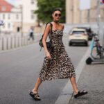 Eine junge Frau in einem leichten, luftigen Kleid mit Leopardenmuster überquert die Straße