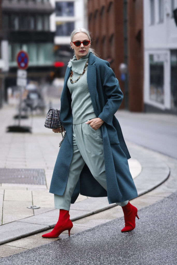 Frau trägt einen benzinfarbenen Mantel und rote Schuhe
